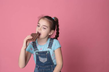 smiling happy girl in a great cheerful mood eating sweet treats chocolate on a bright pink background