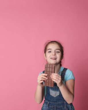 smiling happy girl in a great cheerful mood eating sweet treats chocolate on a bright pink background