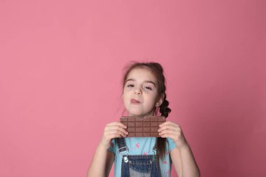 smiling happy girl in a great cheerful mood eating sweet treats chocolate on a bright pink background
