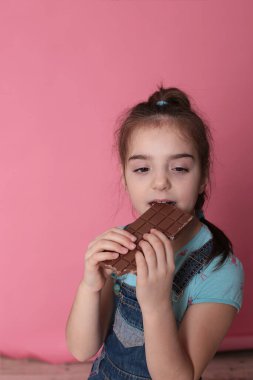 smiling happy girl in a great cheerful mood eating sweet treats chocolate on a bright pink background
