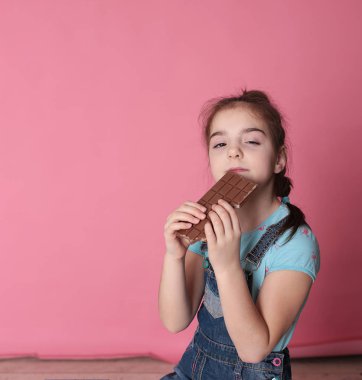 smiling happy girl in a great cheerful mood eating sweet treats chocolate on a bright pink background