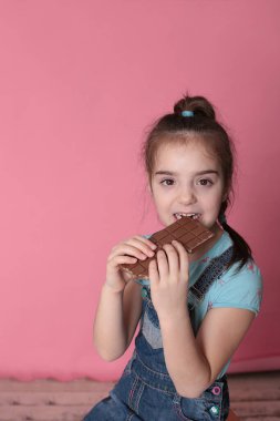 smiling happy girl in a great cheerful mood eating sweet treats chocolate on a bright pink background