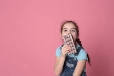 smiling happy girl in a great cheerful mood eating sweet treats chocolate on a bright pink background