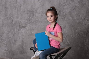 funny girl of eight years old holds a colored sheet of paper free space for writing on a bright background