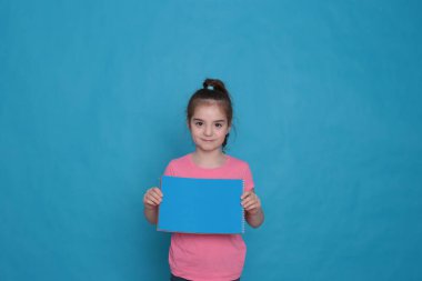 funny girl of eight years old holds a colored sheet of paper free space for writing on a bright background