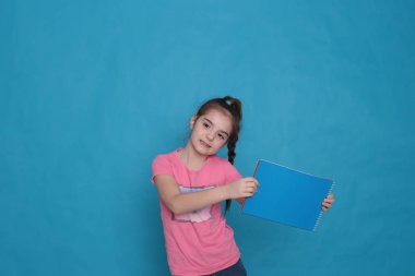 funny girl of eight years old holds a colored sheet of paper free space for writing on a bright background