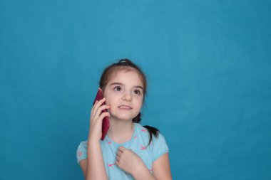 A smiling girl of eight years old holds a pink telephone in her hands on a blue background