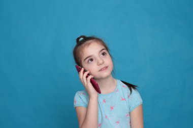 A smiling girl of eight years old holds a pink telephone in her hands on a blue background