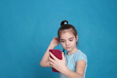 A smiling girl of eight years old holds a pink telephone in her hands on a blue background