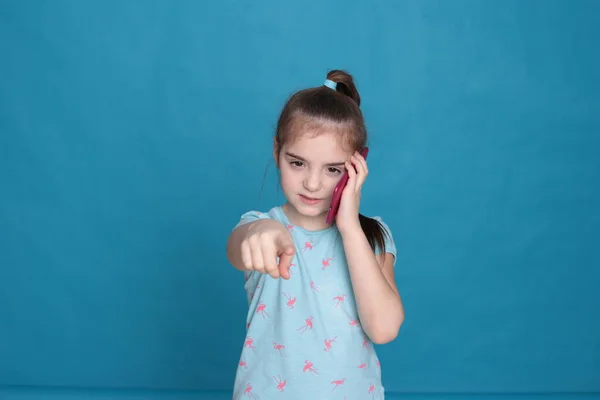 A smiling girl of eight years old holds a pink telephone in her hands on a blue background