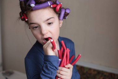 Sekiz yaşında güzel, neşeli bir kız uzun saçlarıyla bigudiler çeviriyor.