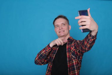 Siyah tişörtlü, parlak mavi arka planlı, kareli tişörtlü şık, şık, şık bir genç portresi.