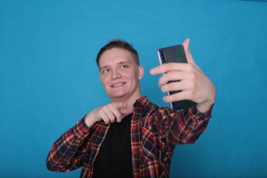 Siyah tişörtlü, parlak mavi arka planlı, kareli tişörtlü şık, şık, şık bir genç portresi.