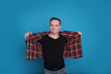 Siyah tişörtlü, parlak mavi arka planlı, kareli tişörtlü şık, şık, şık bir genç portresi.