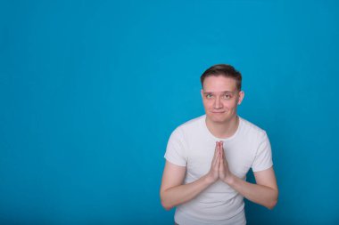 Beyaz tişörtlü komik, yakışıklı genç bir adamın şık portresi. Parlak mavi arka planda mükemmel bir ruh hali içinde.