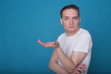 Beyaz tişörtlü komik, yakışıklı genç bir adamın şık portresi. Parlak mavi arka planda mükemmel bir ruh hali içinde.