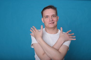 Beyaz tişörtlü komik, yakışıklı genç bir adamın şık portresi. Parlak mavi arka planda mükemmel bir ruh hali içinde.