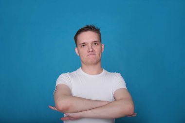 Beyaz tişörtlü komik, yakışıklı genç bir adamın şık portresi. Parlak mavi arka planda mükemmel bir ruh hali içinde.