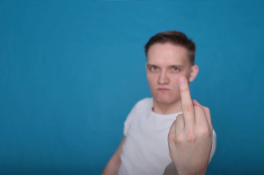 Beyaz tişörtlü komik, yakışıklı genç bir adamın şık portresi. Parlak mavi arka planda mükemmel bir ruh hali içinde.