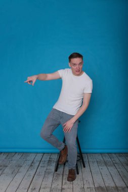 Beyaz tişörtlü komik, yakışıklı genç bir adamın şık portresi. Parlak mavi arka planda mükemmel bir ruh hali içinde.