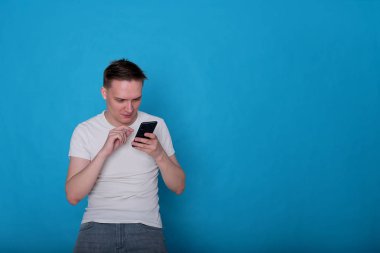 Beyaz tişörtlü komik, yakışıklı genç bir adamın şık portresi. Parlak mavi arka planda mükemmel bir ruh hali içinde.