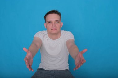 Beyaz tişörtlü komik, yakışıklı genç bir adamın şık portresi. Parlak mavi arka planda mükemmel bir ruh hali içinde.