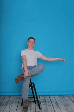 Beyaz tişörtlü komik, yakışıklı genç bir adamın şık portresi. Parlak mavi arka planda mükemmel bir ruh hali içinde.