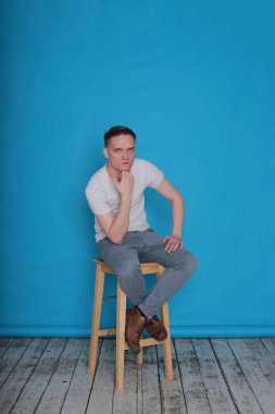 Modern portre duygusal klas, beyaz tişörtlü, parlak mavi arka planlı genç adam.