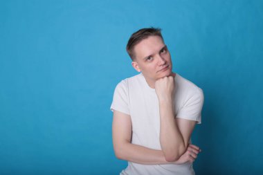 Modern portre duygusal klas, beyaz tişörtlü, parlak mavi arka planlı genç adam.