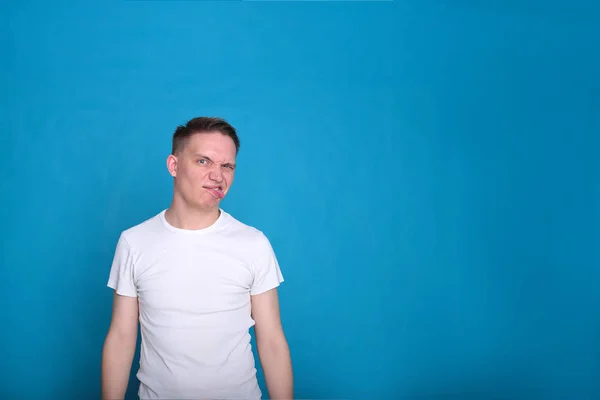 stylish portrait of a funny handsome young guy in a white T-shirt in excellent mood on a bright blue background