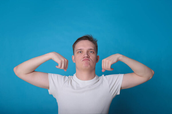 stylish portrait of a funny handsome young guy in a white T-shirt in excellent mood on a bright blue background