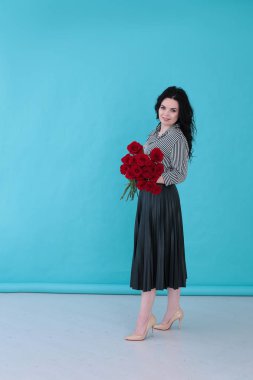 Parlak turkuaz arka planda çizgili bluzu ve pileli eteği olan güzel genç bir kadın.