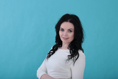 30 yıllık kıvırcık siyah saçlı ve sulu turkuaz arka planda beyaz elbiseli bir kadın.