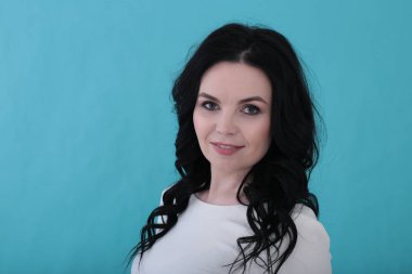 30 yıllık kıvırcık siyah saçlı ve sulu turkuaz arka planda beyaz elbiseli bir kadın.