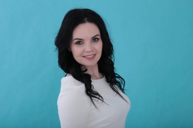 30 yıllık kıvırcık siyah saçlı ve sulu turkuaz arka planda beyaz elbiseli bir kadın.