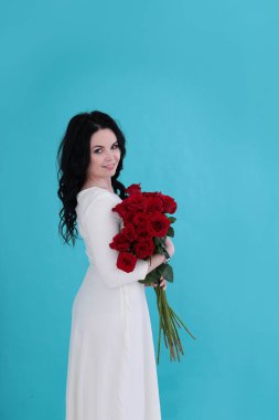 30 yıllık kıvırcık siyah saçlı ve sulu turkuaz arka planda beyaz elbiseli bir kadın.