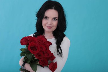 30 yıllık kıvırcık siyah saçlı ve sulu turkuaz arka planda beyaz elbiseli bir kadın.