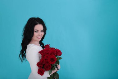 30 yıllık kıvırcık siyah saçlı ve sulu turkuaz arka planda beyaz elbiseli bir kadın.