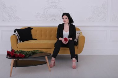  30 yaşındaki kadın iyi bir ruh hali içinde pantolon giymiş, sarı bir koltukta oturuyor.