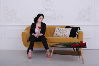  30 yaşındaki kadın iyi bir ruh hali içinde pantolon giymiş, sarı bir koltukta oturuyor.