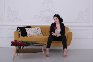  30 yaşındaki kadın iyi bir ruh hali içinde pantolon giymiş, sarı bir koltukta oturuyor.