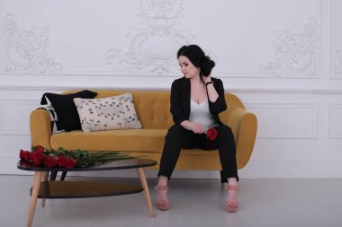  30 yaşındaki kadın iyi bir ruh hali içinde pantolon giymiş, sarı bir koltukta oturuyor.