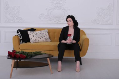  30 yaşındaki kadın iyi bir ruh hali içinde pantolon giymiş, sarı bir koltukta oturuyor.