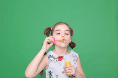 Sekiz yaşında, komik saç stili, çiçekli mavi bir bluz giyen, elinde bir şişeyle oynayan, sabun köpüğü üfleyen, çocukların eğlencesine katılan komik bir kız.