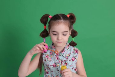 Sekiz yaşında, komik saç stili, çiçekli mavi bir bluz giyen, elinde bir şişeyle oynayan, sabun köpüğü üfleyen, çocukların eğlencesine katılan komik bir kız.