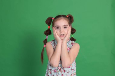 Havalı, genç ve güzel bir kız, sekiz yaşında, harika bir ruh hali içinde, mavi bluzlu, çiçekli, parlak yeşil bir arka planda hoş bir saç stili var.