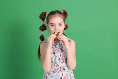 Sekiz yaşında güzel bir kız, komik bir saç stili, harika bir ruh hali içinde, parlak yeşil bir arka planda kurabiyeli çikolata yiyor.