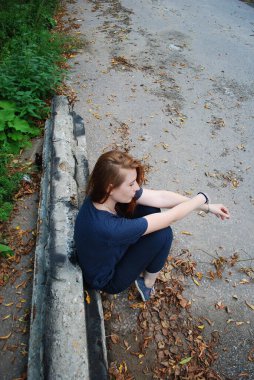 Üzgün, genç, çekici, kızıl saçlı bir kız poposunun üzerinde oturmuş kaldırım taşına yaslanıyor. Kız düşünür, düşüncelere dalar..