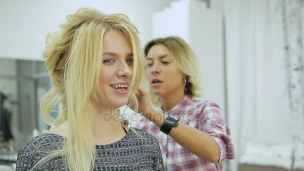 Парикмахер делает прическу молодой блондинке в салоне красоты — стоковое видео