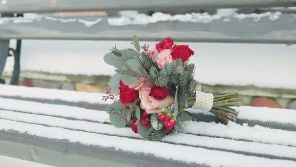 Свадебный букет, лежащий на снежной скамейке — стоковое видео